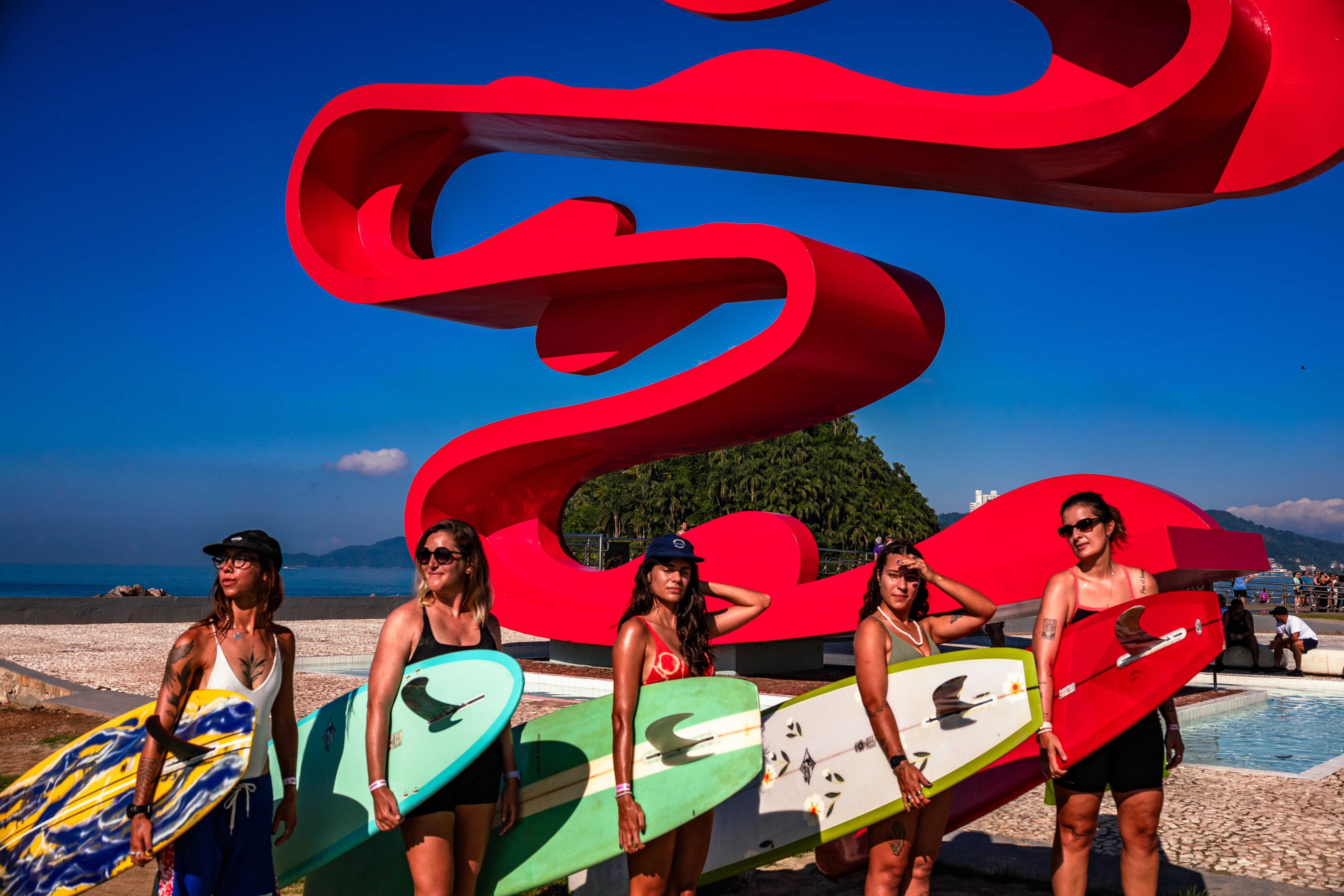 Grupo de surfistas com pranchas coloridas em frente à escultura vermelha