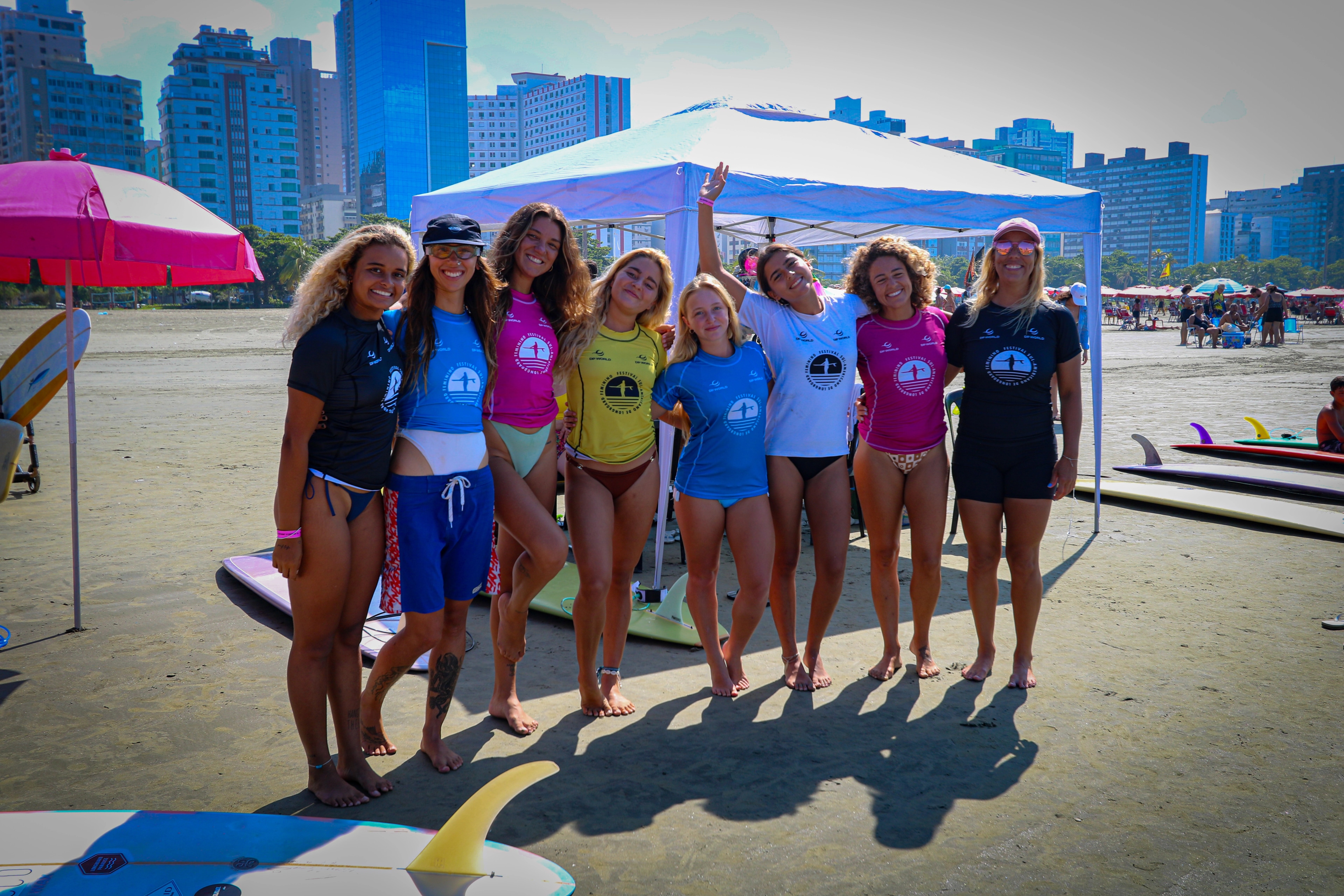 Grupo de competidoras reunidas na praia com a cidade ao fundo