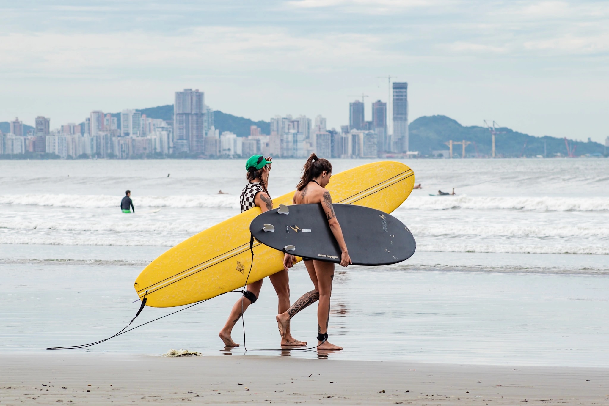 Duas surfistas caminhando com longboards à beira-mar